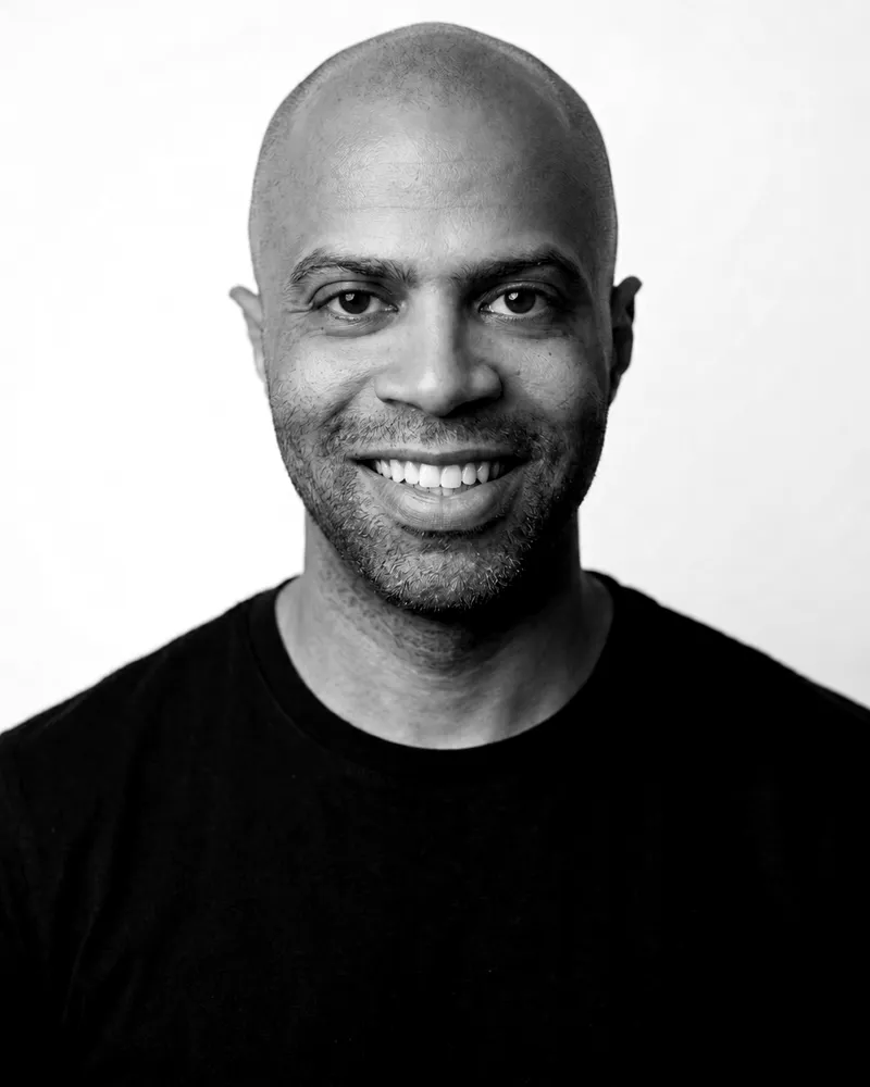 Vinicius Garutti sorrindo, de camiseta preta, em retrato preto e branco