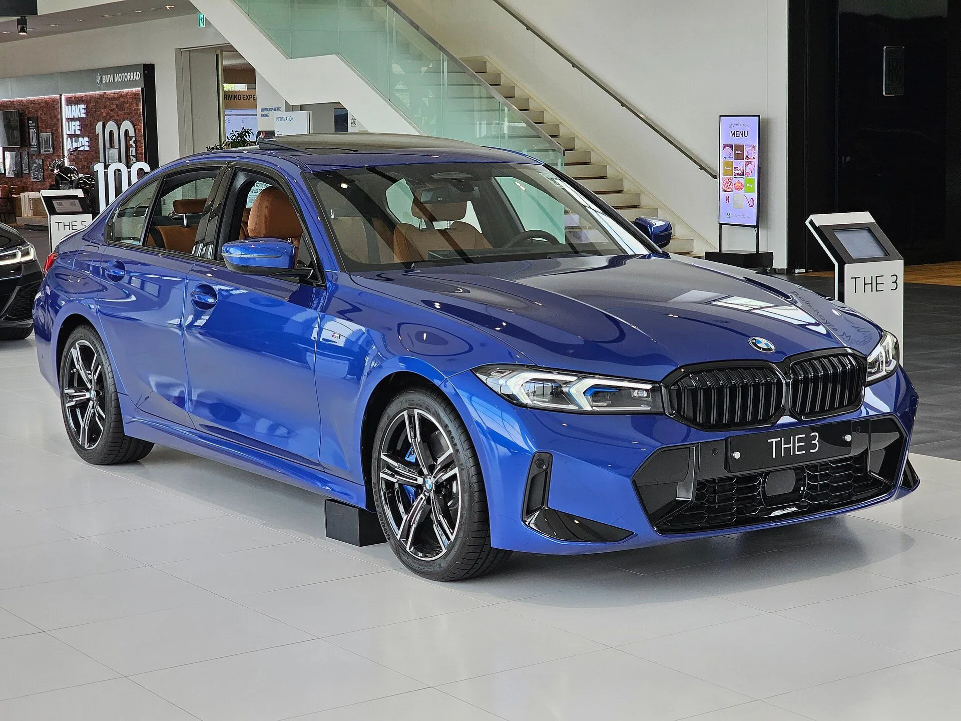 BMW 320i M Sport azul da linha reestilizada em showroom, vista dianteira três-quartos