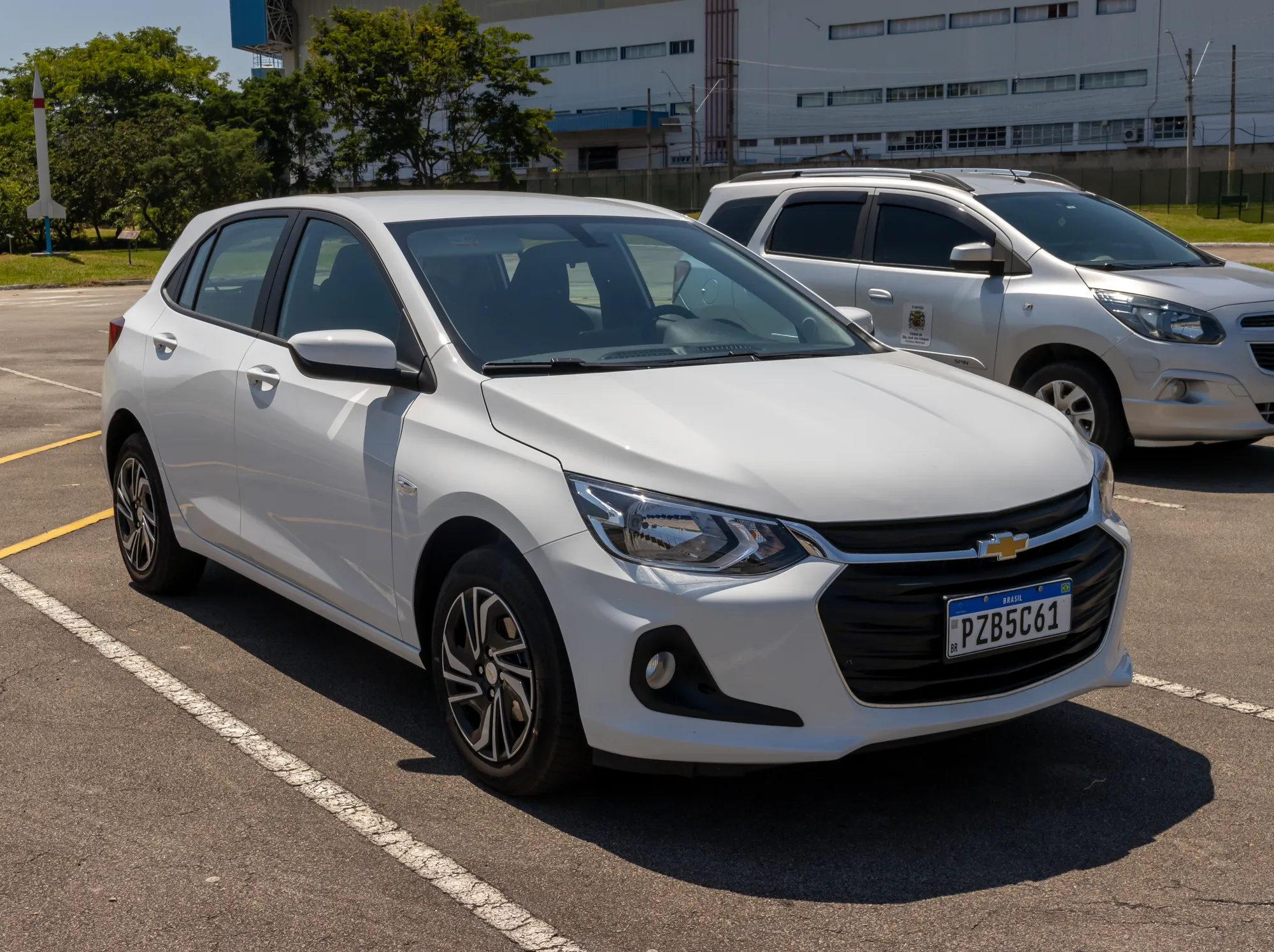 Chevrolet Onix hatch branco de segunda geração estacionado, visto pela frente e pela lateral