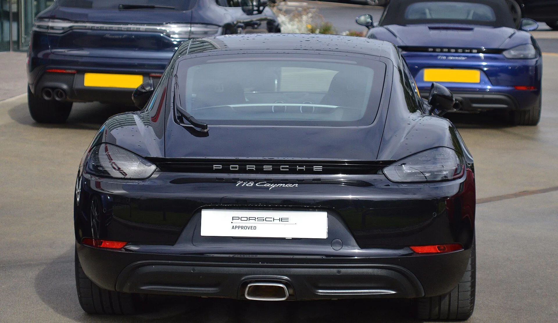 Traseira do Porsche 718 Cayman preto em pátio de concessionária